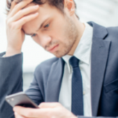 <p>頭を抱えながらスマホ操作する男性</p>
